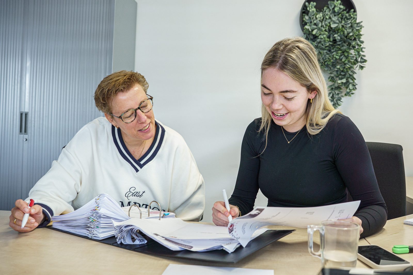 Silvia (links) en Marise (rechts) van de administratie nemen samen een dossier door